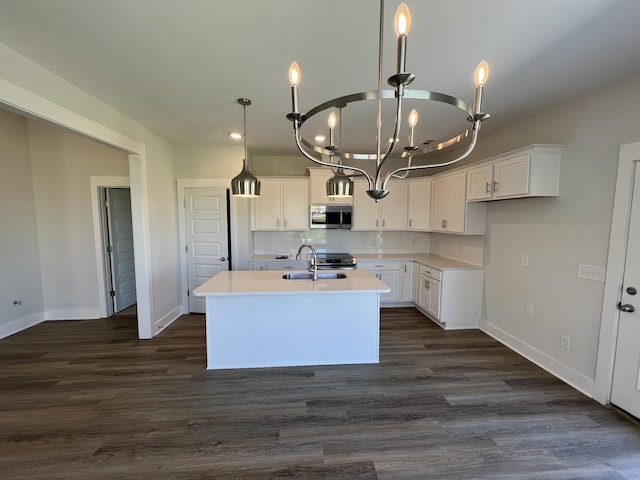 kitchen with appliances with stainless steel finishes, white cabinetry, backsplash, hanging light fixtures, and a kitchen island with sink