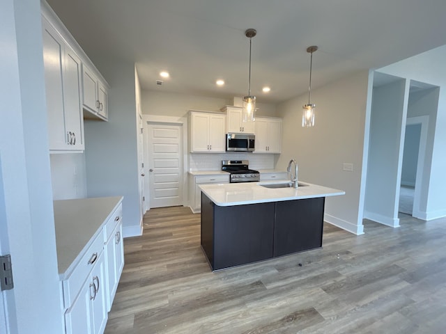 kitchen with appliances with stainless steel finishes, decorative light fixtures, sink, white cabinetry, and a center island with sink