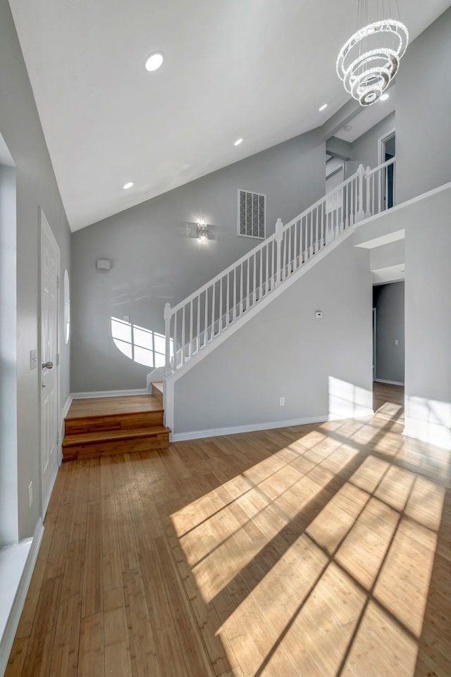 unfurnished living room featuring light wood-type flooring, a towering ceiling, and a notable chandelier