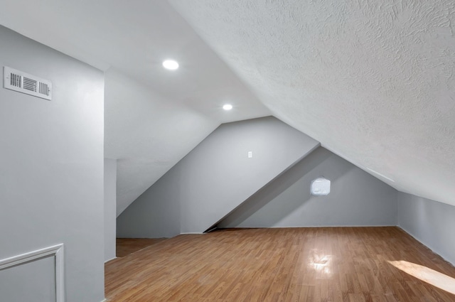 additional living space with wood-type flooring, a textured ceiling, and vaulted ceiling