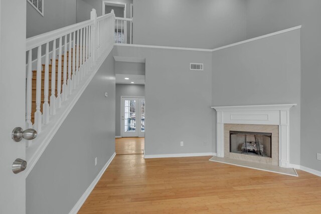 unfurnished living room with a premium fireplace, a towering ceiling, ornamental molding, and light hardwood / wood-style floors