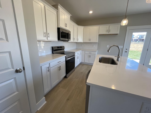 kitchen featuring white cabinets, appliances with stainless steel finishes, sink, hanging light fixtures, and a center island with sink