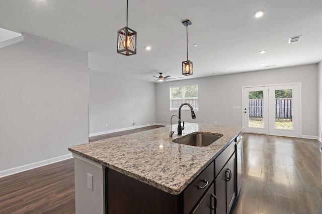 kitchen with sink, a center island with sink, decorative light fixtures, and light stone countertops