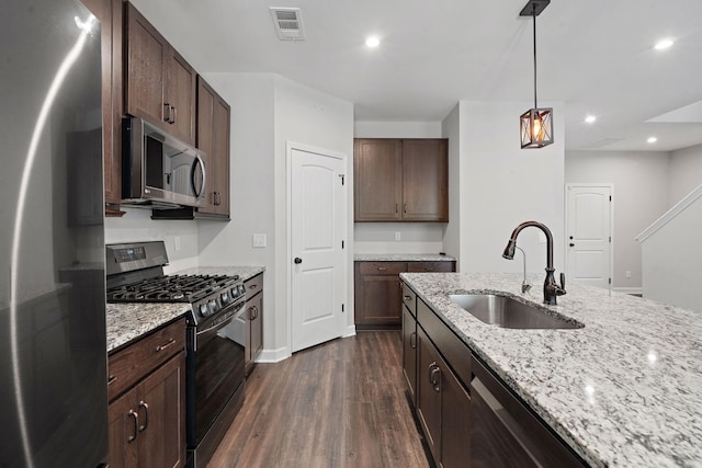 kitchen with pendant lighting, appliances with stainless steel finishes, sink, light stone counters, and dark brown cabinets