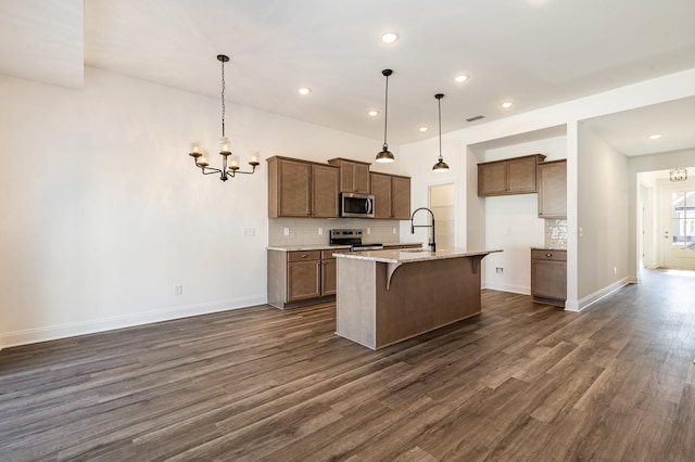 kitchen featuring pendant lighting, a kitchen bar, dark hardwood / wood-style flooring, stainless steel appliances, and a kitchen island with sink