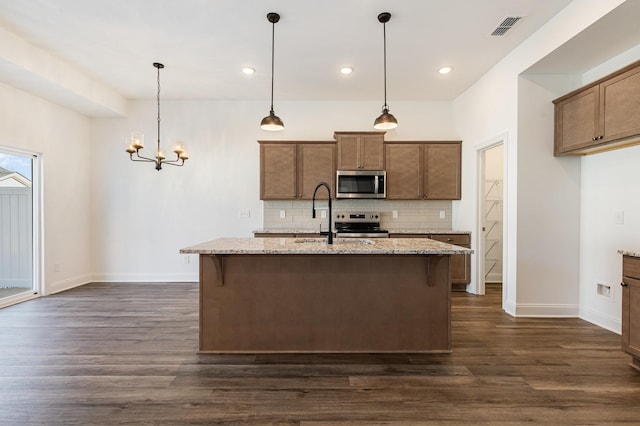 kitchen with sink, pendant lighting, an island with sink, stainless steel appliances, and light stone counters