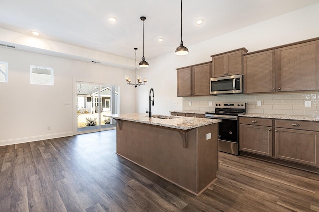 kitchen with light stone countertops, sink, pendant lighting, stainless steel appliances, and a center island with sink