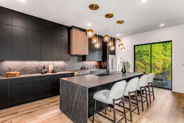 kitchen with decorative backsplash, an island with sink, modern cabinets, decorative light fixtures, and a sink