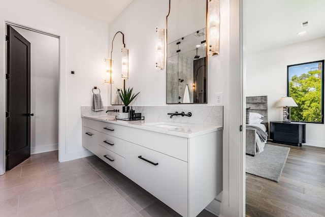 ensuite bathroom with double vanity, a stall shower, a sink, ensuite bath, and baseboards