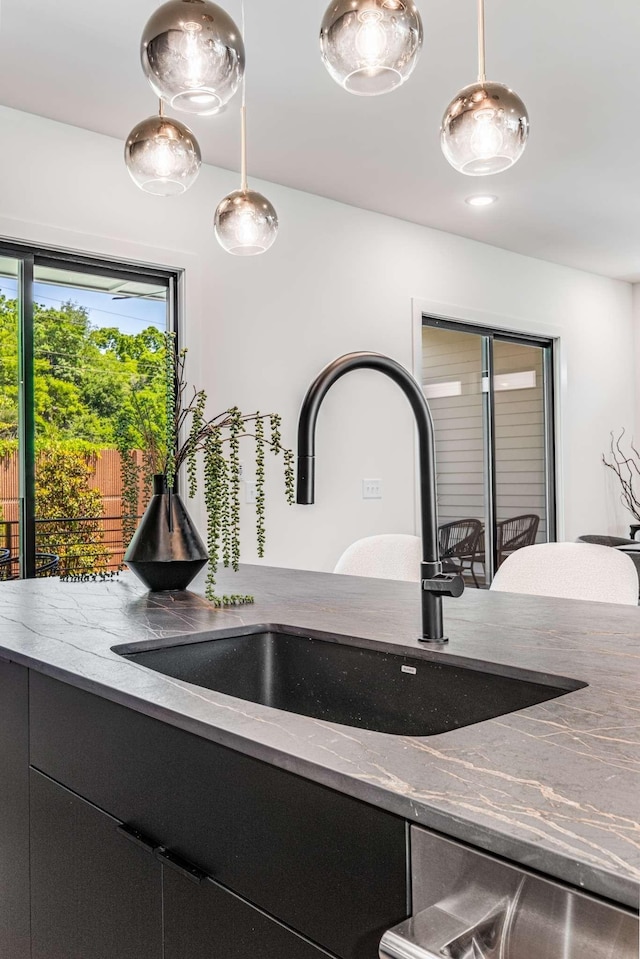 room details featuring a sink, hanging light fixtures, dark cabinetry, light stone countertops, and dishwasher