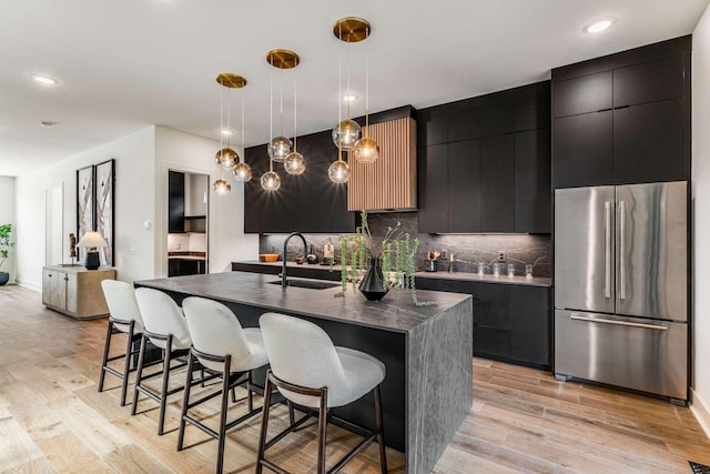 kitchen with a sink, freestanding refrigerator, light wood finished floors, a center island with sink, and pendant lighting