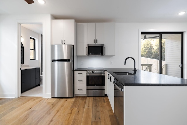 kitchen with dark countertops, white cabinetry, appliances with stainless steel finishes, and a sink