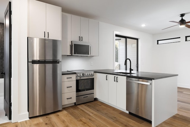 kitchen featuring stainless steel appliances, dark countertops, white cabinetry, and a sink