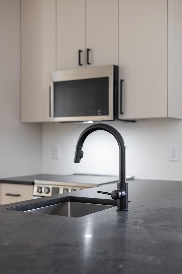 details with dark countertops, white cabinetry, stainless steel microwave, and a sink