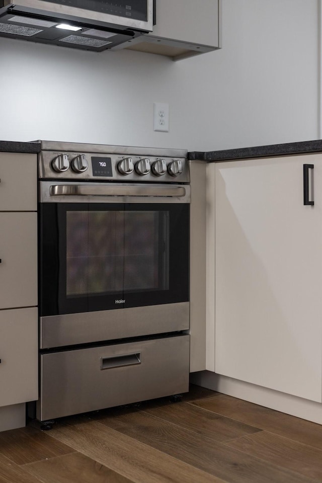 kitchen with stainless steel appliances, dark countertops, dark wood-style flooring, and white cabinets