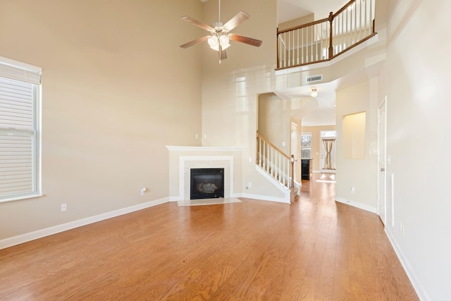 unfurnished living room with ceiling fan, a high ceiling, and light hardwood / wood-style flooring