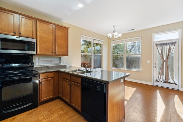 kitchen with a wealth of natural light, black appliances, light hardwood / wood-style floors, sink, and kitchen peninsula