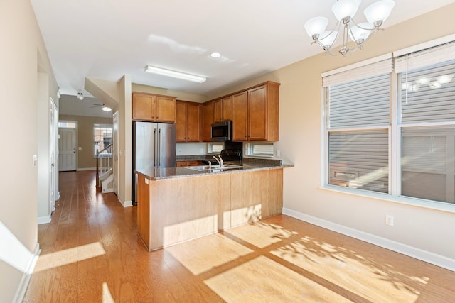 kitchen with appliances with stainless steel finishes, dark stone counters, kitchen peninsula, a chandelier, and light wood-type flooring