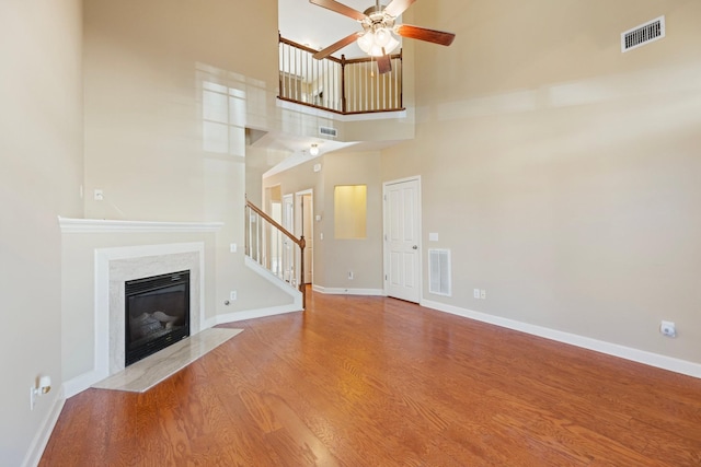 unfurnished living room featuring light wood-type flooring, a towering ceiling, a high end fireplace, and ceiling fan