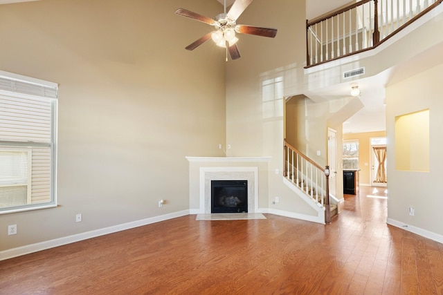 unfurnished living room featuring hardwood / wood-style floors, a towering ceiling, and ceiling fan