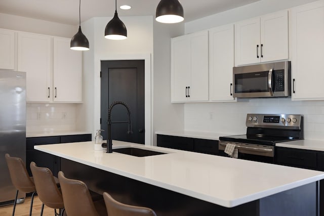 kitchen with decorative light fixtures, white cabinets, stainless steel appliances, and an island with sink