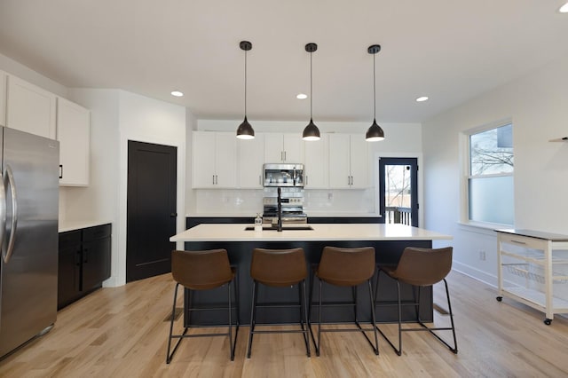 kitchen featuring decorative light fixtures, a kitchen island with sink, white cabinetry, and appliances with stainless steel finishes