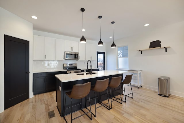 kitchen featuring white cabinetry, an island with sink, stainless steel appliances, and hanging light fixtures