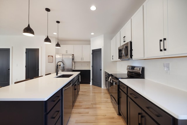 kitchen featuring white cabinetry, appliances with stainless steel finishes, a kitchen island with sink, and hanging light fixtures