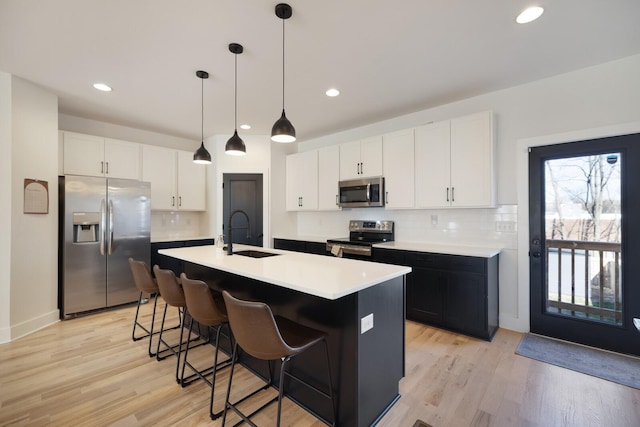 kitchen featuring appliances with stainless steel finishes, decorative light fixtures, white cabinetry, sink, and a center island with sink