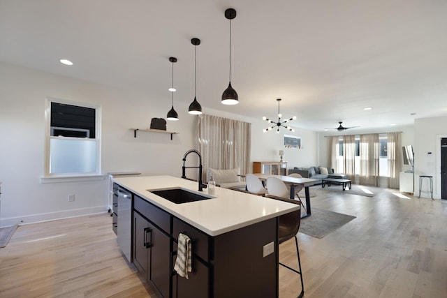 kitchen with pendant lighting, sink, a kitchen island with sink, stainless steel dishwasher, and light hardwood / wood-style flooring