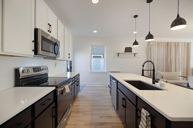 kitchen featuring appliances with stainless steel finishes, decorative light fixtures, white cabinetry, sink, and light hardwood / wood-style flooring