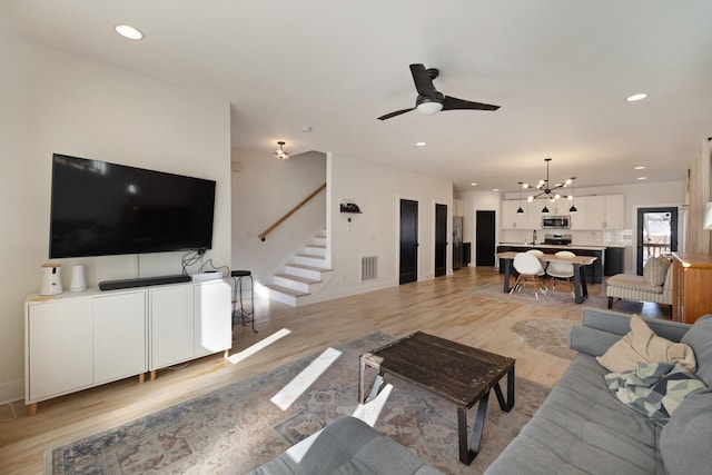 living room with light wood-type flooring and ceiling fan with notable chandelier