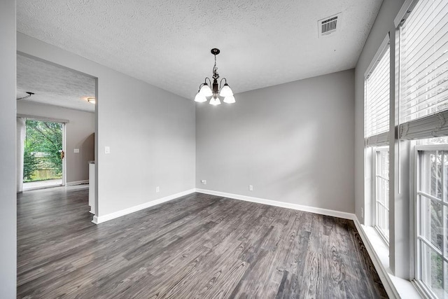 empty room with dark wood-type flooring, a textured ceiling, and a notable chandelier