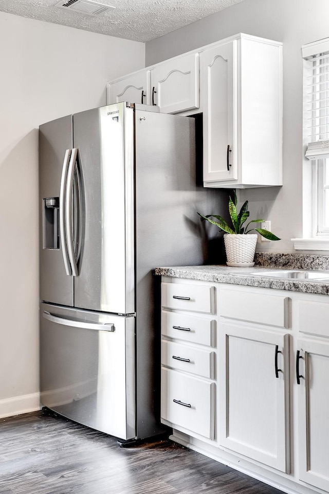 kitchen with stainless steel refrigerator with ice dispenser, a textured ceiling, white cabinets, and dark hardwood / wood-style floors