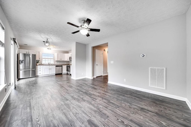 unfurnished living room featuring ceiling fan, a textured ceiling, and dark hardwood / wood-style flooring