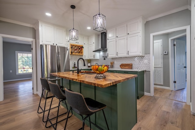 kitchen featuring butcher block countertops, sink, white cabinetry, a kitchen island with sink, and wall chimney exhaust hood