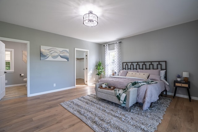 bedroom featuring hardwood / wood-style flooring, a walk in closet, ensuite bathroom, and multiple windows