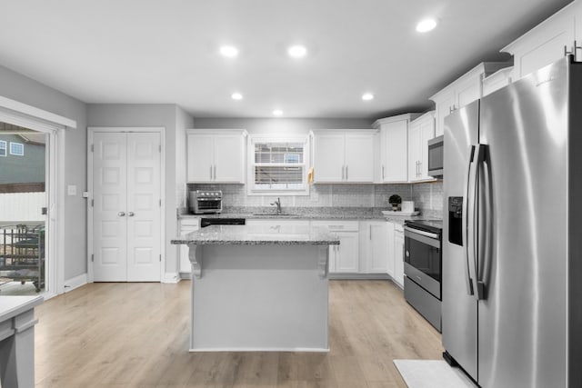 kitchen with light stone countertops, appliances with stainless steel finishes, white cabinets, a kitchen island, and sink