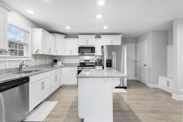 kitchen featuring a kitchen island, light stone counters, white cabinetry, and stainless steel appliances