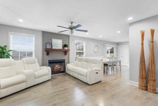 living room with a fireplace, light wood-type flooring, and ceiling fan