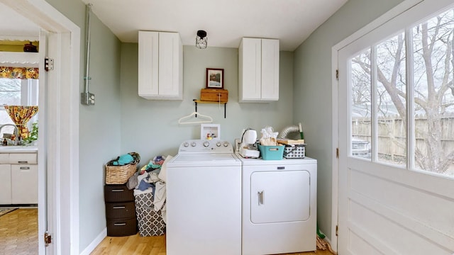 clothes washing area with washing machine and clothes dryer, a wealth of natural light, light hardwood / wood-style flooring, and cabinets