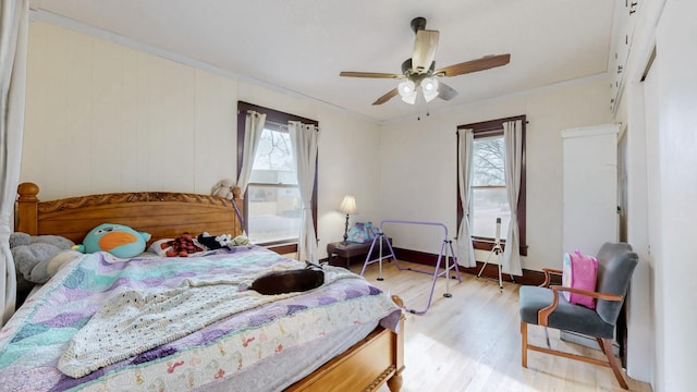 bedroom featuring a ceiling fan, light wood-type flooring, multiple windows, and crown molding