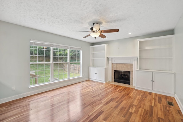 unfurnished living room with ceiling fan, light hardwood / wood-style flooring, a fireplace, and a textured ceiling