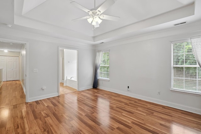 unfurnished bedroom with ceiling fan, multiple windows, and a tray ceiling