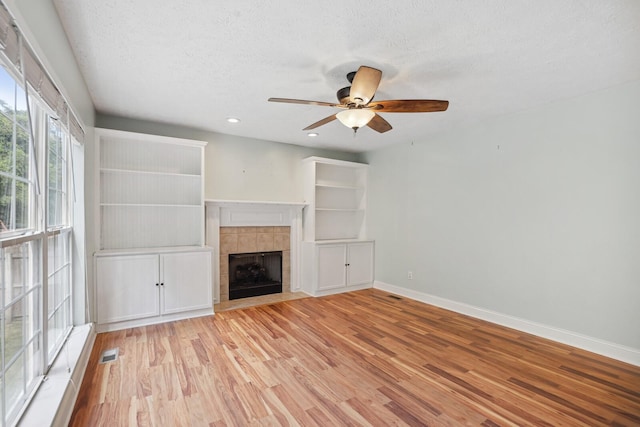 unfurnished living room with light hardwood / wood-style floors, a textured ceiling, ceiling fan, and a fireplace