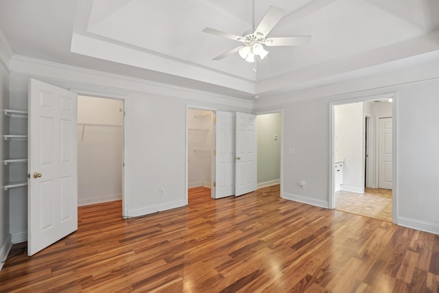 unfurnished bedroom featuring a walk in closet, hardwood / wood-style flooring, a raised ceiling, ornamental molding, and ceiling fan