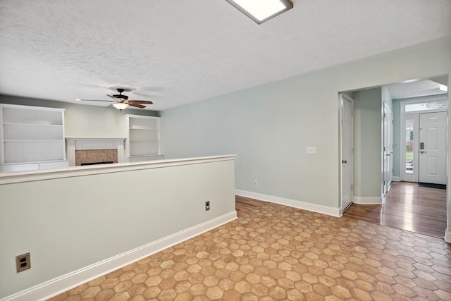 unfurnished room with ceiling fan, a textured ceiling, and a fireplace