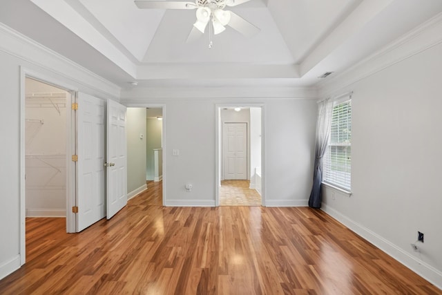 unfurnished bedroom featuring crown molding, ceiling fan, a raised ceiling, hardwood / wood-style floors, and a walk in closet