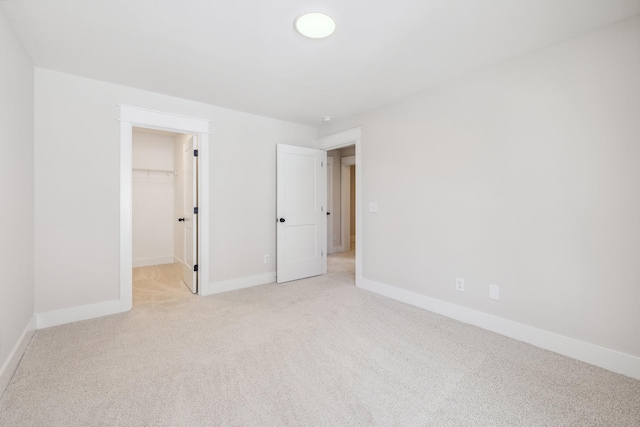 unfurnished bedroom with a spacious closet, a closet, and light carpet