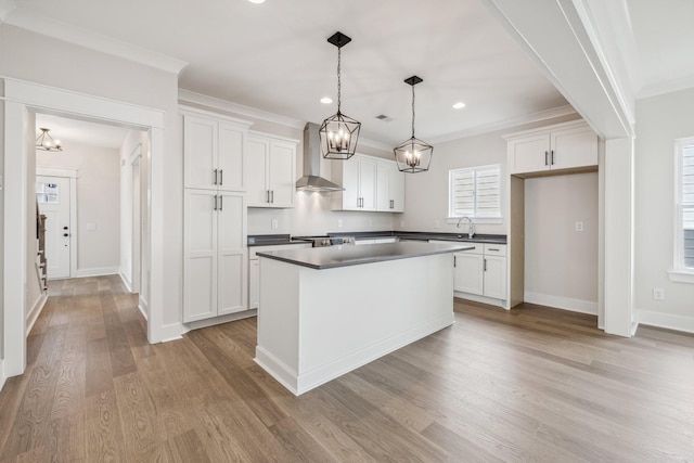 kitchen with wall chimney exhaust hood, decorative light fixtures, white cabinets, sink, and a kitchen island